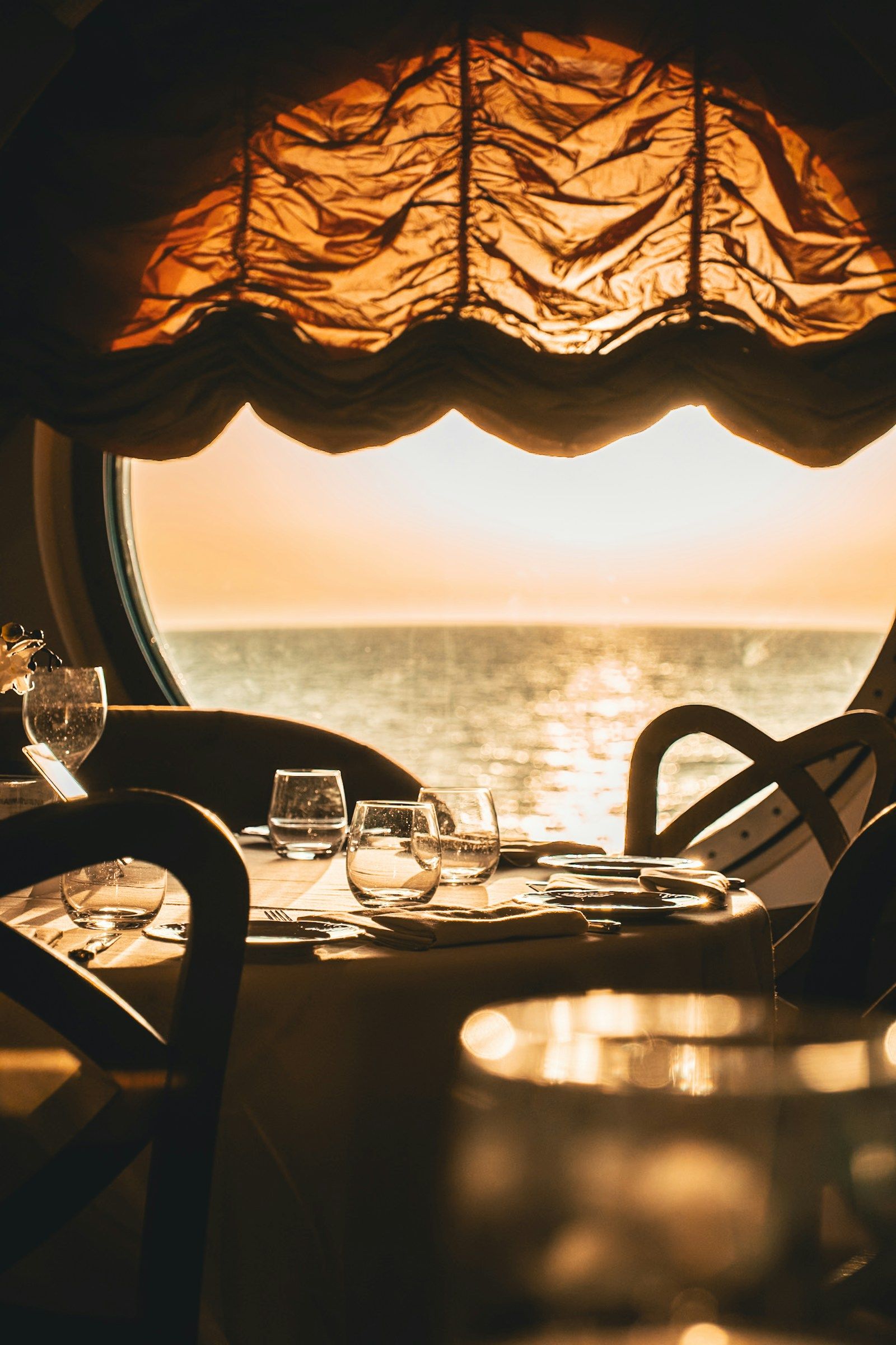 A dining table set for dinner, looking out over the sea at sunset.