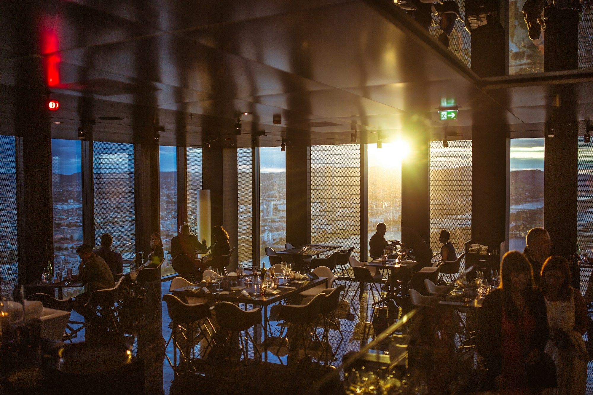 Guests at dinner in a restaurant with floor-to-ceiling windows, the sun setting between the columns.