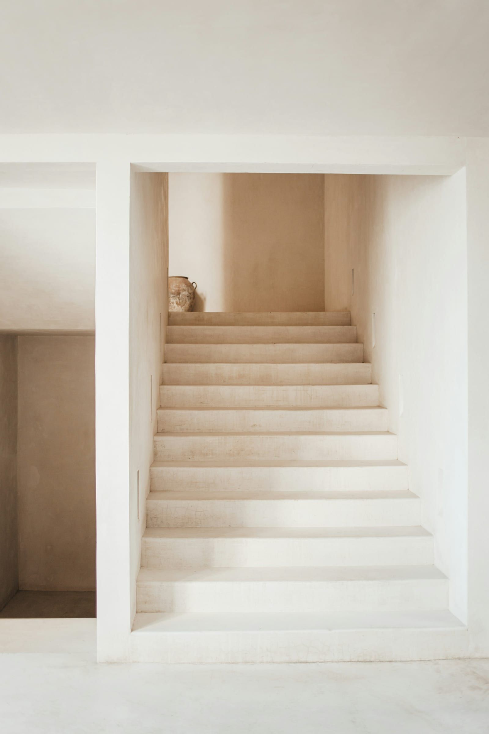 Pale lime-washed stairs rising to a landing with a single clay vase.